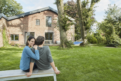 Lächelndes, liebevolles Paar, das im Garten seines Hauses sitzt, lizenzfreies Stockfoto