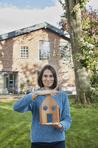 Portrait of smiling woman in garden of her home holding house model stock photo