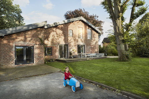 Mädchen spielt mit Seifenkiste in der Einfahrt eines Wohnhauses, lizenzfreies Stockfoto