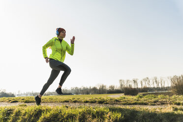 Young woman with headphones running on rural path - UUF13046