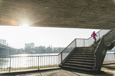 Young woman running up stairs at a river - UUF13053