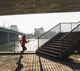 Junge Frau läuft auf eine Treppe an einem Fluss zu - UUF13054