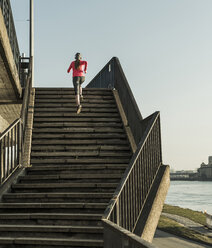 Junge Frau läuft eine Treppe an einem Fluss hinauf - UUF13056