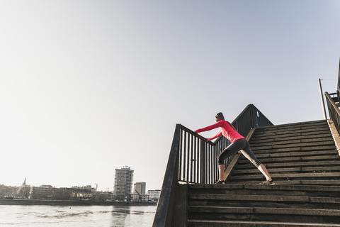 Young woman stretching on stairs at a river in the city stock photo