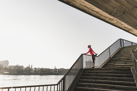 Young woman stretching on stairs at a river in the city stock photo