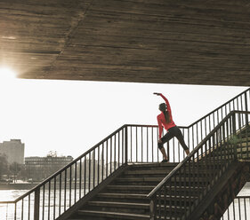 Young woman stretching on stairs at a river in the city - UUF13059