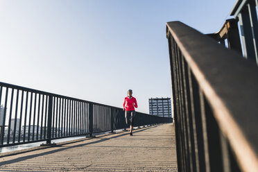 Junge Frau läuft auf einer Brücke in der Stadt - UUF13062