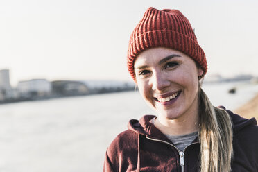 Porträt einer lächelnden, sportlichen jungen Frau am Flussufer in der Stadt - UUF13071