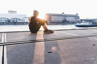 Sportliche junge Frau bei einer Pause am Flussufer in der Stadt bei Sonnenuntergang - UUF13079