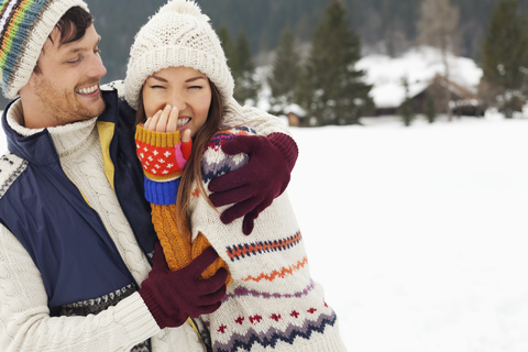 Lachendes und sich umarmendes Paar im verschneiten Feld, lizenzfreies Stockfoto