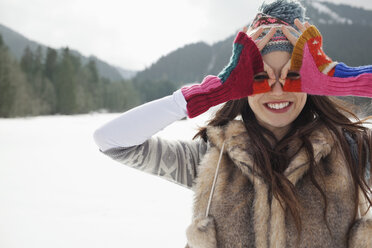 Porträt einer lächelnden Frau, die mit den Fingern in einem verschneiten Feld um die Augen kreist - CAIF12356