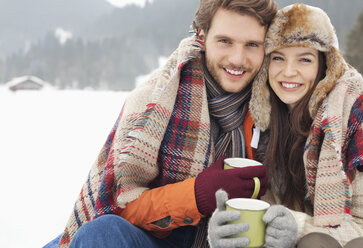 Porträt eines glücklichen Paares beim Kaffeetrinken in einem verschneiten Feld - CAIF12358