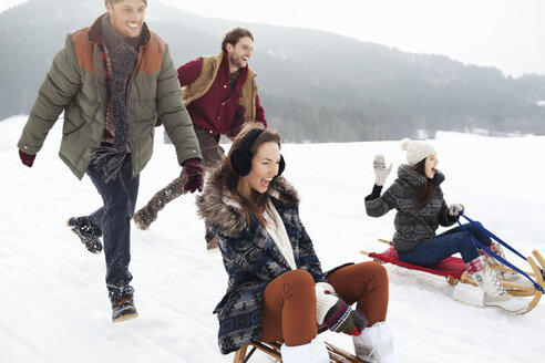 Begeisterte Freunde beim Schlittenfahren auf einem verschneiten Feld - CAIF12362