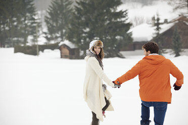 Glückliches Paar, das sich an den Händen hält und in einem verschneiten Feld spazieren geht - CAIF12363