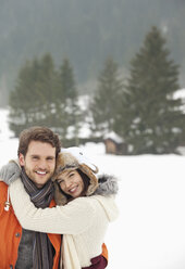 Porträt eines lächelnden, sich umarmenden Paares in einem verschneiten Feld - CAIF12372