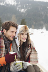 Happy couple drinking coffee in snowy field - CAIF12374