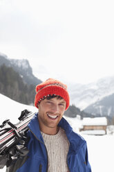 Nahaufnahme eines lächelnden Mannes mit Skiern in einem verschneiten Feld - CAIF12381