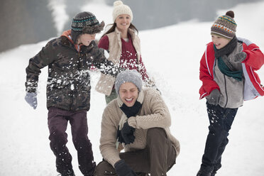 Playful family enjoying snowball fight in field - CAIF12391