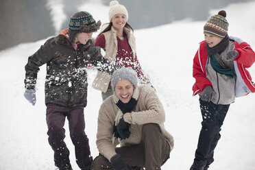 Verspielte Familie bei einer Schneeballschlacht auf einem Feld - CAIF12391