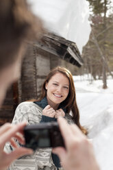 Man photographing smiling woman in snow outside cabin - CAIF12397