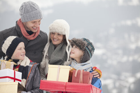 Glückliche Familie mit Weihnachtsgeschenken im Schnee - CAIF12398