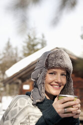 Nahaufnahme Porträt einer Frau mit Pelzmütze, die vor einer Hütte Kaffee trinkt - CAIF12401