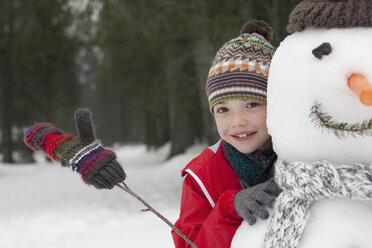 Nahaufnahme eines lächelnden Jungen hinter einem Schneemann - CAIF12406