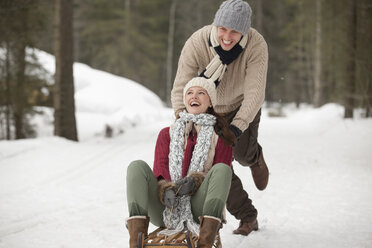 Happy couple sledding in snowy field - CAIF12407