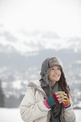 Smiling woman drinking coffee in snowy field - CAIF12409