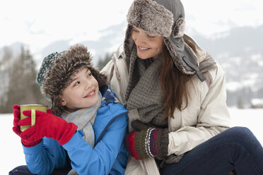 Happy mother and son drinking hot chocolate in snowy field - CAIF12410