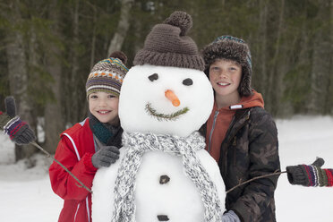 Porträt eines glücklichen Jungen, der mit einem Schneemann posiert - CAIF12413