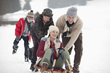 Glückliche Familie beim Schlittenfahren im verschneiten Feld - CAIF12414