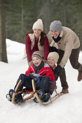 Glückliche Familie beim Schlittenfahren im verschneiten Wald - CAIF12426