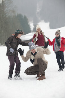 Glückliche Familie bei einer Schneeballschlacht auf einem Feld - CAIF12427