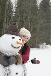 Glückliche Frau, die einen Schneemann im Wald umarmt - CAIF12432