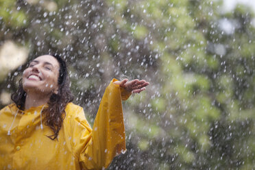 Happy woman standing with arms outstretched in rain - CAIF12448