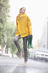 Happy woman dancing barefoot in rainy street - CAIF12450