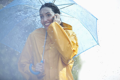 Glückliche Frau, die unter einem Regenschirm mit ihrem Handy telefoniert - CAIF12451