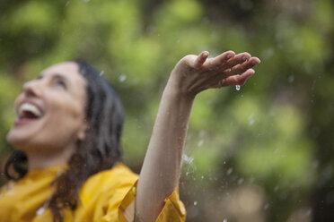 Enthusiastic woman standing with arms outstretched and head back in rain - CAIF12453