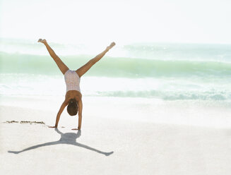 Girl doing cartwheel on beach - CAIF12464