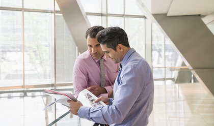 Corporate businessmen reviewing paperwork in modern office lobby - CAIF12474