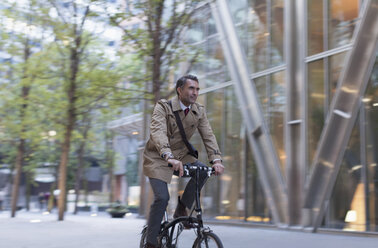 Geschäftsmann fährt Fahrrad vor einem modernen Gebäude - CAIF12484