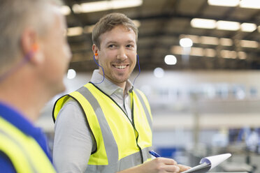 Vorgesetzter mit Klemmbrett, der einen Arbeiter in einer Stahlfabrik anlächelt - CAIF12486