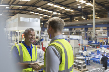 Smiling supervisor and worker handshaking in steel factory - CAIF12570