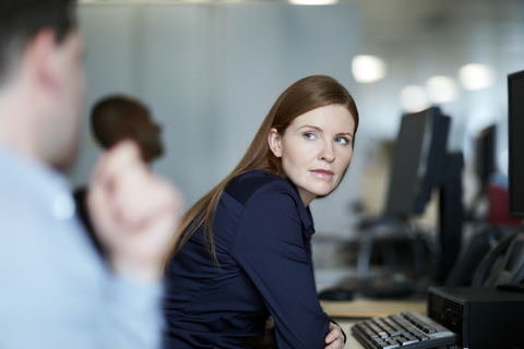 Geschäftsfrau am Computer hört einem Geschäftsmann zu, lizenzfreies Stockfoto