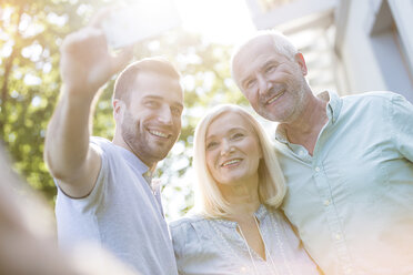 Smiling senior couple and adult son taking selfie outdoors - CAIF12678