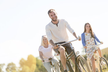 Lächelnder junger Mann beim Fahrradfahren mit Frauen - CAIF12679