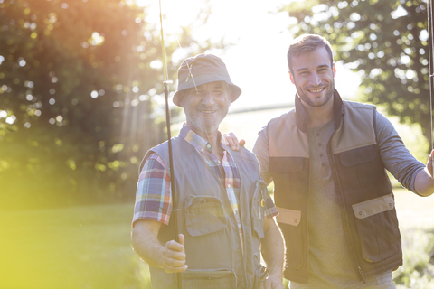 Portrait lächelnder Vater und erwachsener Sohn mit Angelruten, lizenzfreies Stockfoto