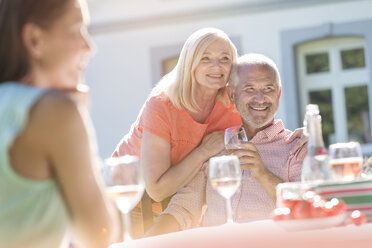 Senior couple smiling and drinking wine on sunny patio - CAIF12694