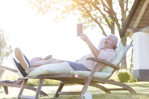 Älterer Mann mit digitalem Tablet, der sich auf einem Liegestuhl im Garten entspannt, lizenzfreies Stockfoto